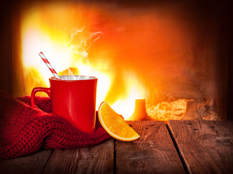 红杯子里的热饮料和陈年木桌上的橘子片-以壁炉为背景-圣诞节或冬季暖饮-具有文本空间的布局