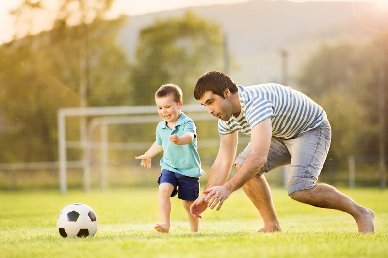 年轻的父亲带着他的小儿子在足球场上踢足球