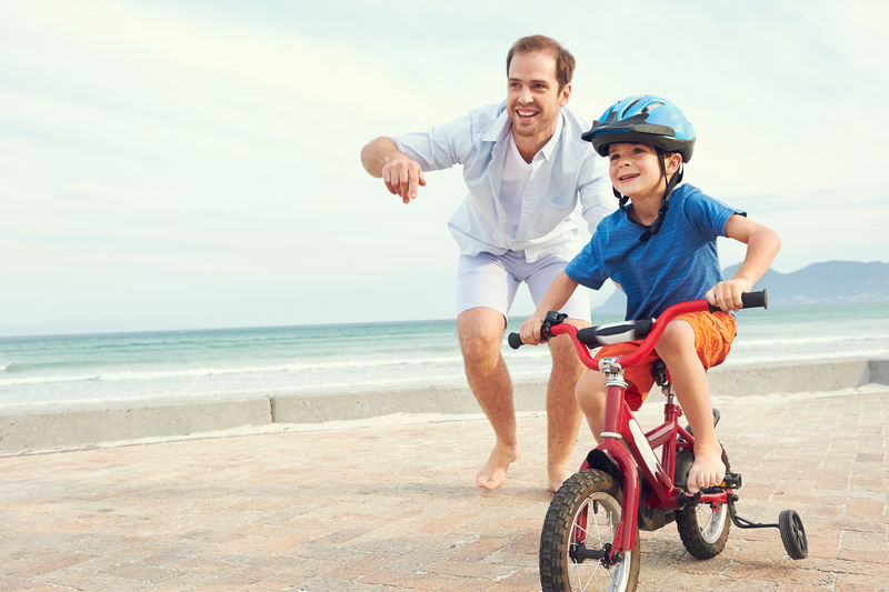 父子俩一起在海边学骑自行车玩得开心