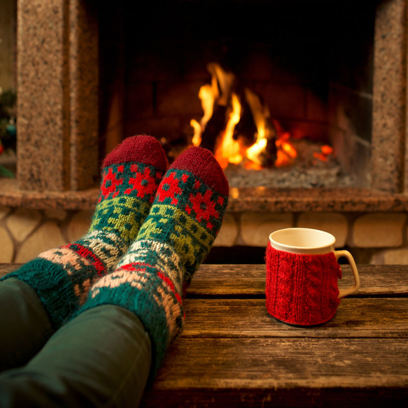 圣诞壁炉内的羊毛袜脚-女人用热火放松-用一杯热饮料-用毛线袜暖脚-双脚靠拢-冬季和圣诞节的概念