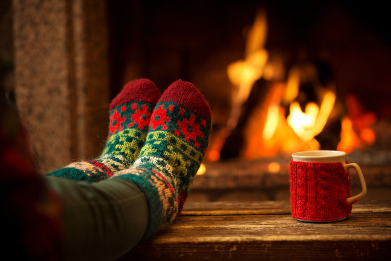 圣诞壁炉内的羊毛袜脚-女人用热火放松-用一杯热饮料-用毛线袜暖脚-双脚靠拢-冬季和圣诞节的概念