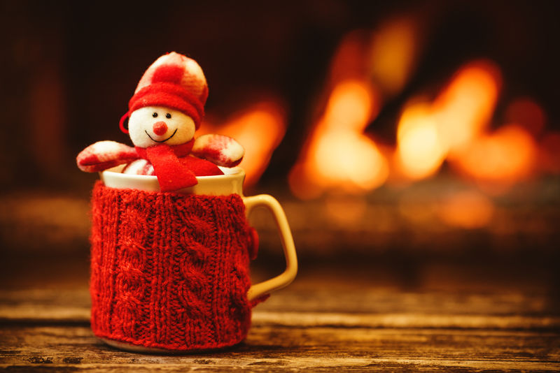在温暖的壁炉前喝一杯热饮料-圣诞节概念-红色针织手套的杯子-饰有雪人玩具-站在炉边-舒适放松的神奇气氛在一个小屋