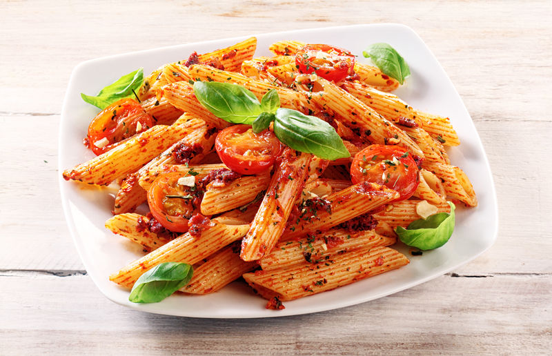 特写的美味可口、辛辣的意大利潘尼通心粉-白盘子里有番茄和香草-放在木桌上