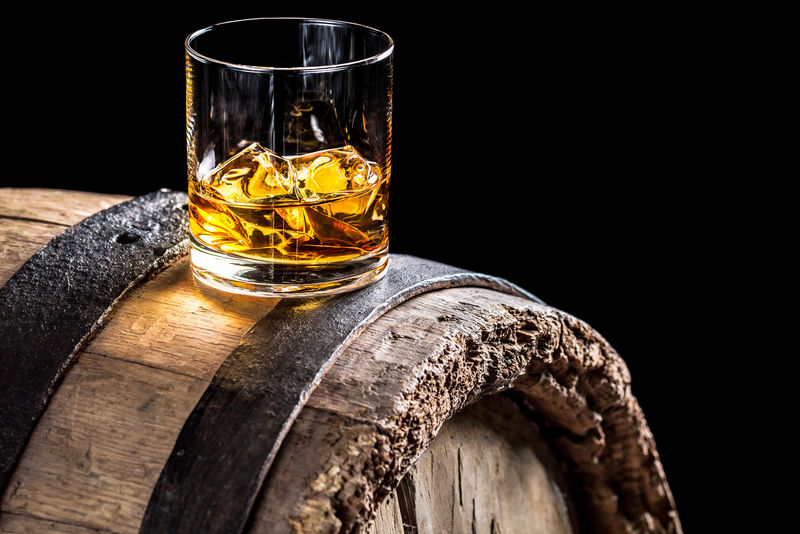 一杯加冰块的威士忌放在旧橡木桶上。