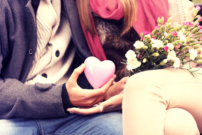 一对情侣坐在公园的长椅上-手里拿着情人节礼物和鲜花