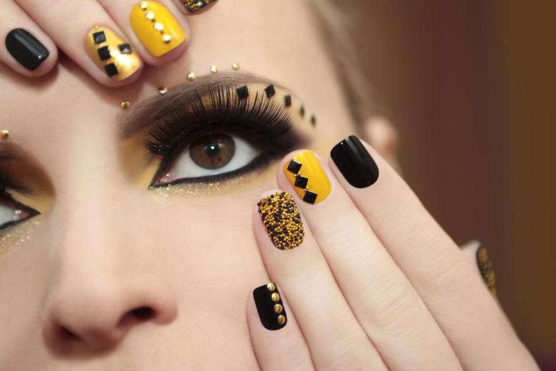 鱼子酱指甲油在黄色和黑色指甲油的女孩假睫毛和不同形状的水钻