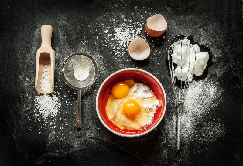 烤蛋糕的配料碗-面粉-鸡蛋-蛋清泡沫-从上面的黑色的黑板打蛋器和蛋壳-烹饪课程或厨房混乱海报概念