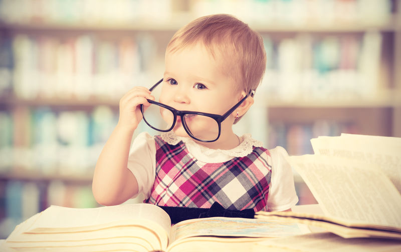 戴眼镜的快乐有趣女婴在图书馆读书