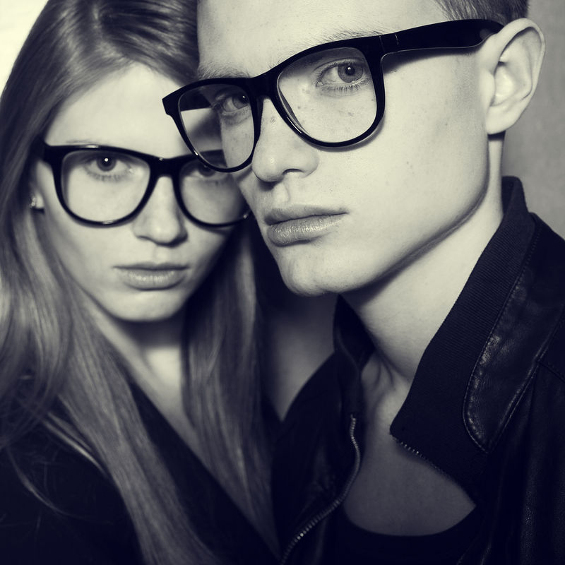 眼镜的概念-金发碧眼的时尚双胞胎-穿着黑色的衣服-戴着时髦的眼镜-在灰色背景下合影-完美的肌肤-时尚风格-闭合.工作室拍摄