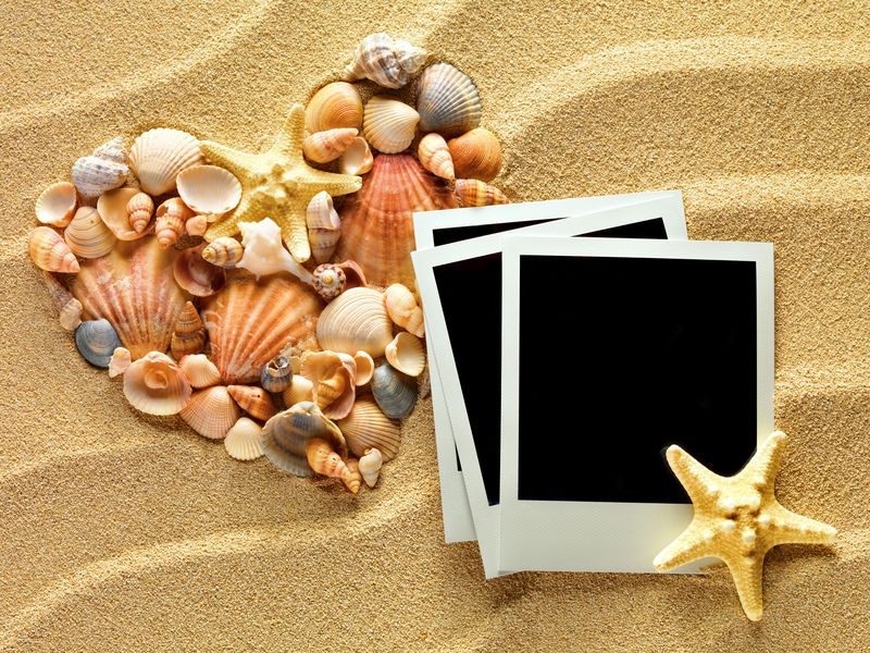 由海贝和海星做成的心躺在沙滩上-上面有老式的空照片卡-夏季风格背景-文本空间