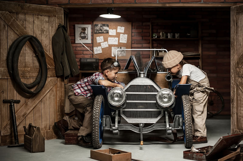 两个男孩站在修理厂旁边-手里拿着复古车
