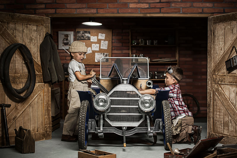 两个男孩站在修理厂旁边-手里拿着复古车