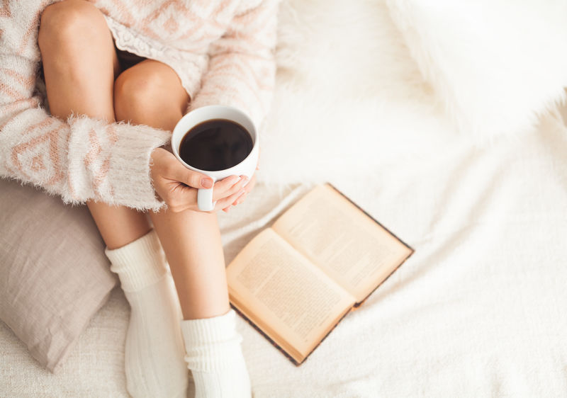 躺在床上的女人拿着一本旧书和一杯咖啡-俯视图