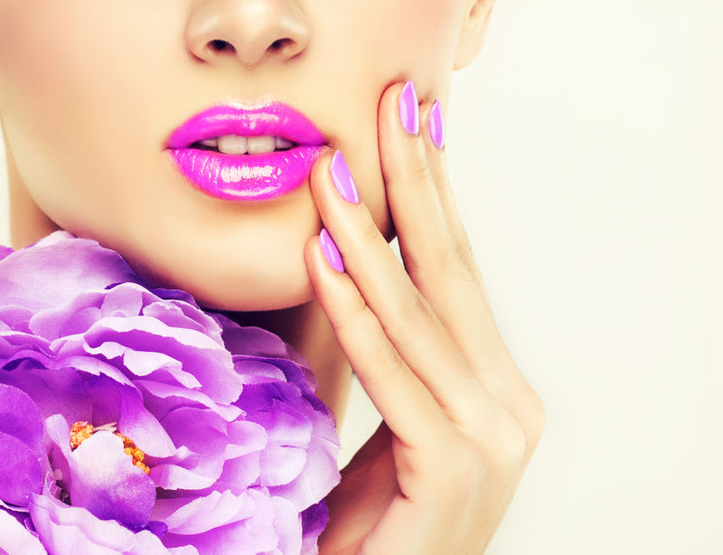 指甲和嘴唇-女人用指甲碰她的脸颊-粉红唇膏和指甲油