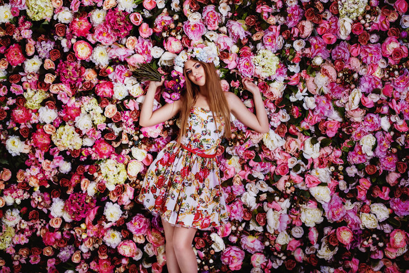 一个美丽的年轻女孩-带着鲜花花束靠近一堵花墙