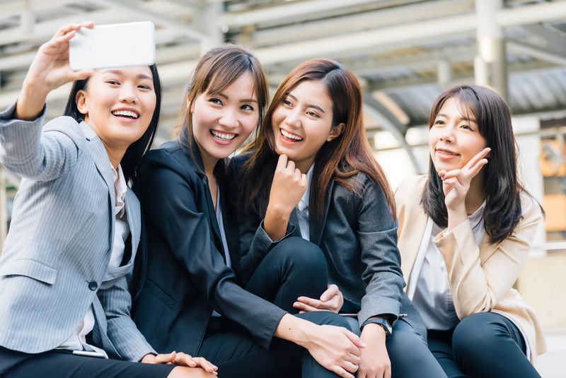 四位快乐的亚洲女商人同事在城市里用智能手机自拍
