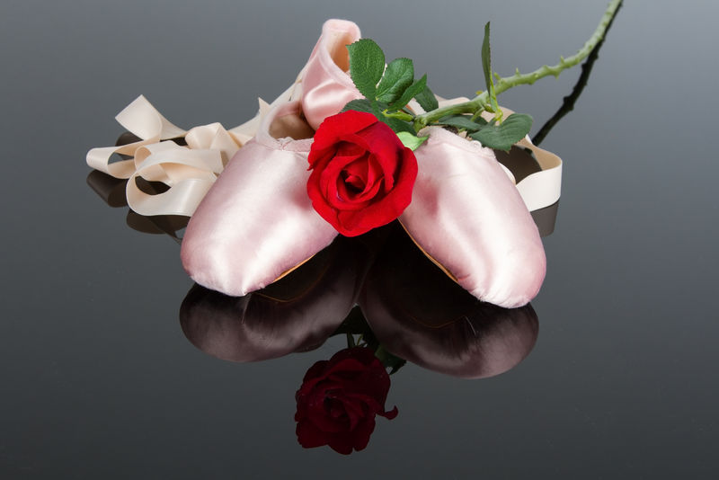 两个芭蕾拖鞋和红玫瑰在闪亮的黑色表面与聚光灯效果