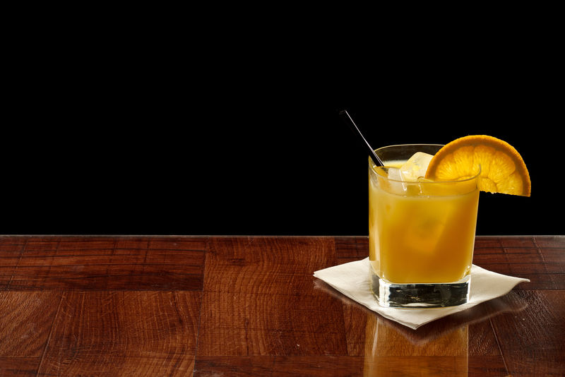 小玻璃杯里的新鲜橙汁-混合伏特加和冰块-在吧台上用黑色隔离