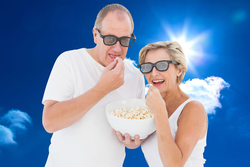 一对戴着3D眼镜的成年夫妇在蓝天白云下吃爆米花
