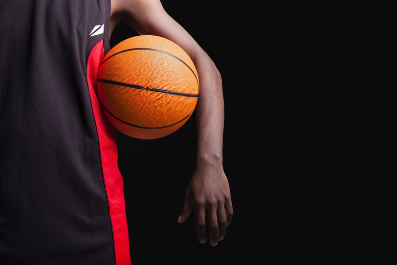 在黑色背景上拿着篮球站着的篮球运动员