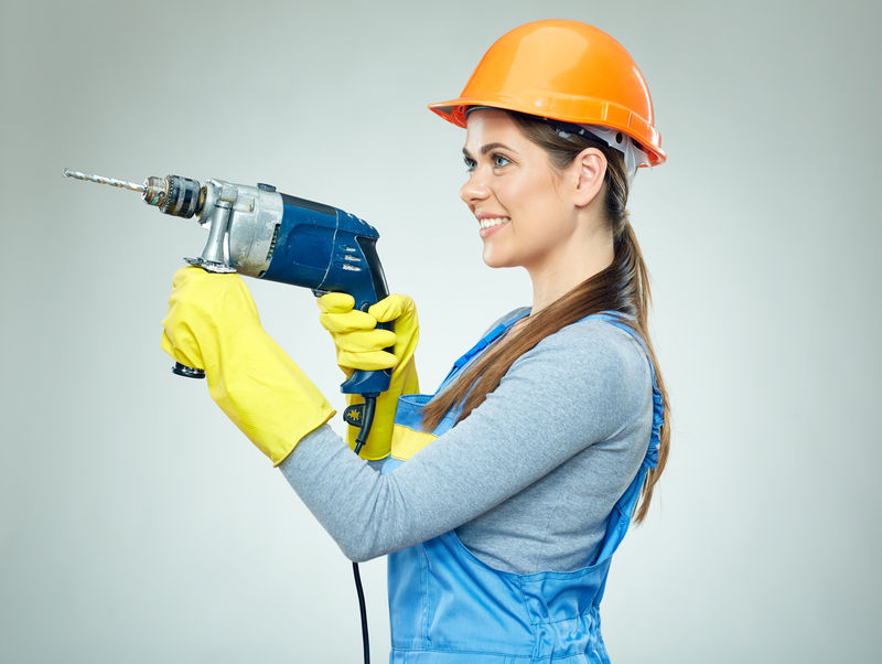 微笑的女建筑工人戴着防护帽，手里拿着统一的钻具。