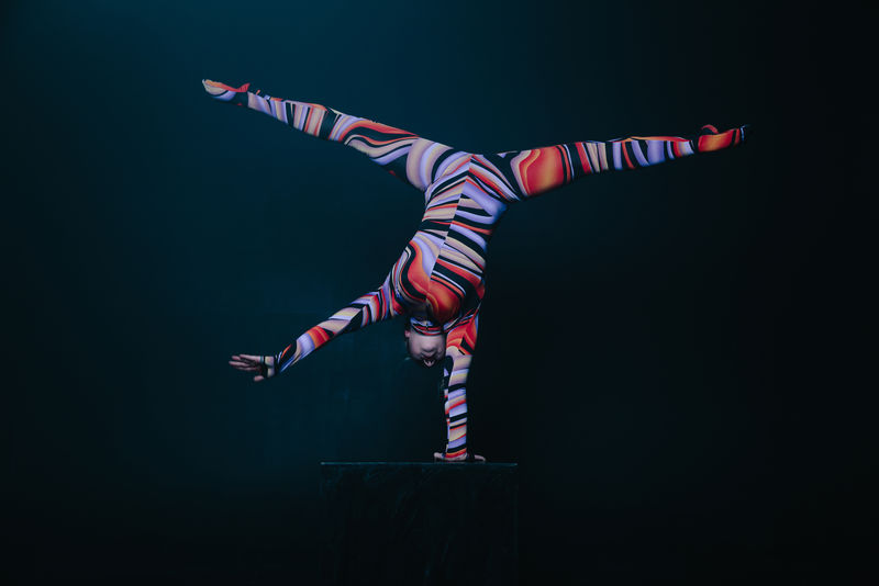 年轻柔韧的金发马戏团杂技演员在演艺厅摆姿势。在立方体上做平衡倒立。
