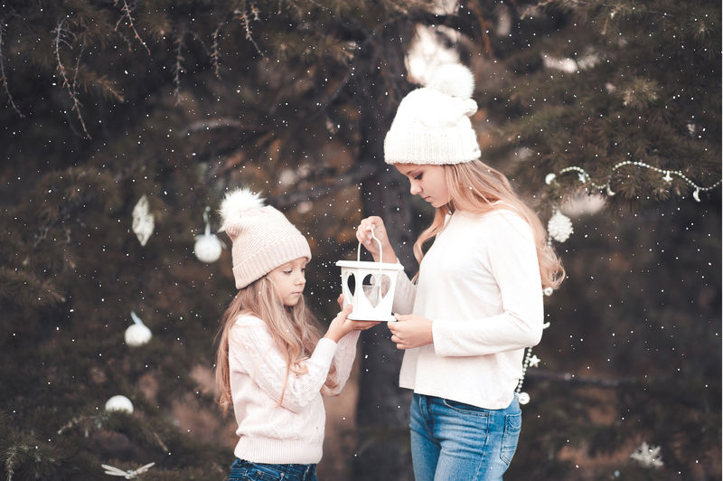 可爱的小女孩穿着针织毛衣，戴着帽子，手里拿着雪地里的白色烛台。看着对方。冬季。