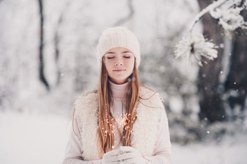 14-16岁的微笑少女，穿着冬季针织衣服，在雪地上拿着闪闪发光的东西。闭上眼睛。圣诞节假期。