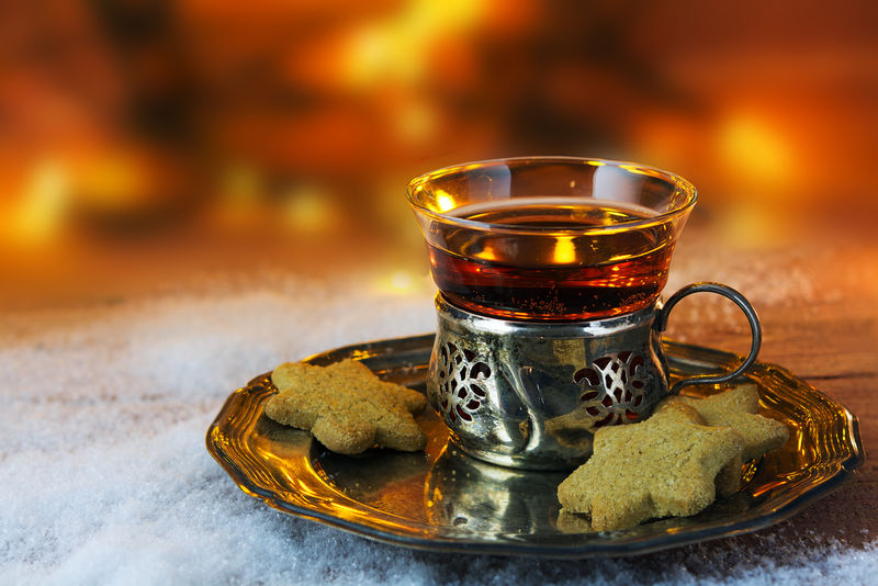 一杯茶和圣诞饼干放在一个银制的老式盘子里，放在雪地里的木头上