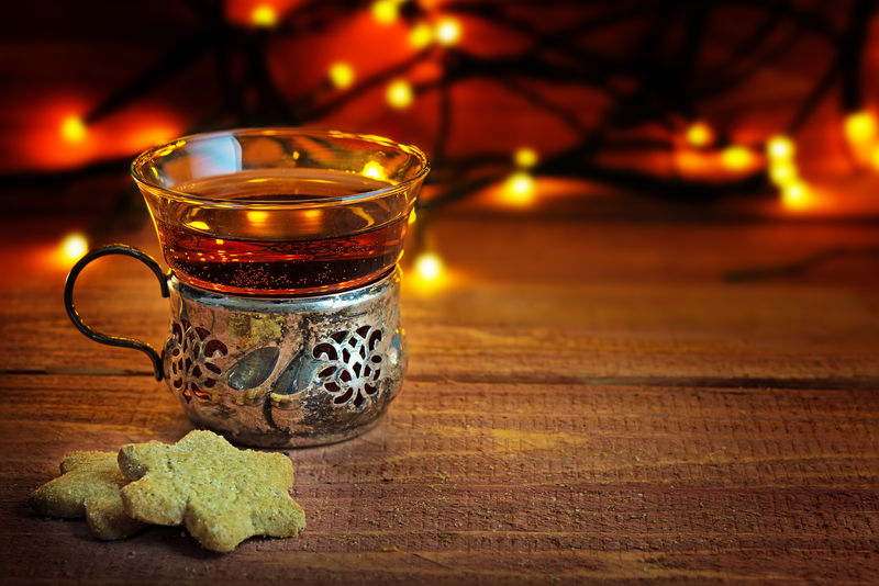 圣诞曲奇和茶放在一个老式的银杯和玻璃杯里，放在乡村的木头上，背景是温暖的灯光。
