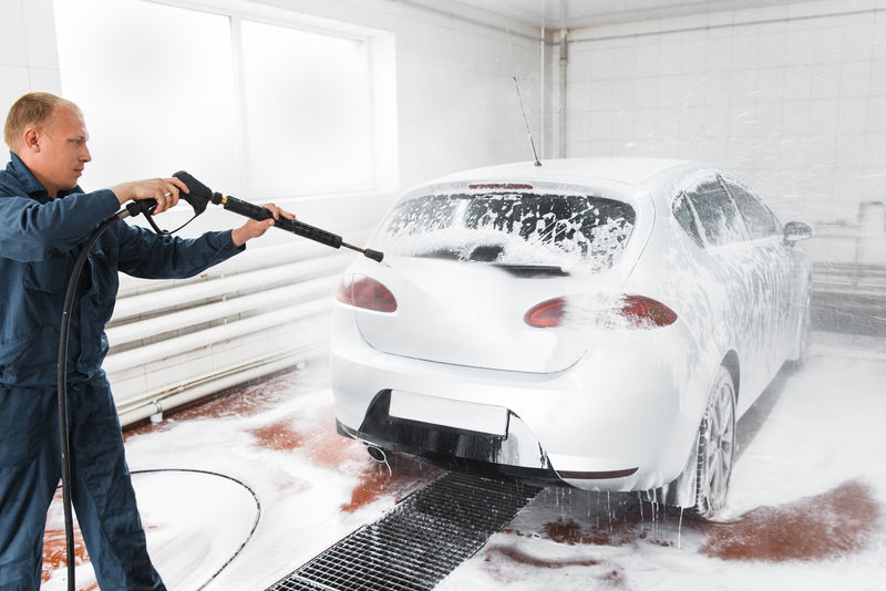 处理洗车的概念，男人在服务站用软管清洗白车。车库工人用鼻子洗汽车