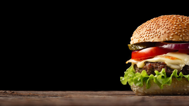 自制汉堡特写镜头与牛肉-西红柿-生菜-奶酪和洋葱在木制桌上-深色背景下的快餐-并为您的文字提供位置