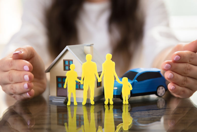 女商人用手保护房子、汽车和桌上的黄色家庭形象