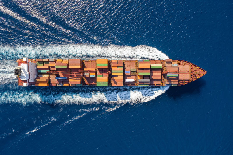 一艘大型集装箱船在蓝海上空航行的俯视图；全球海上货物运输