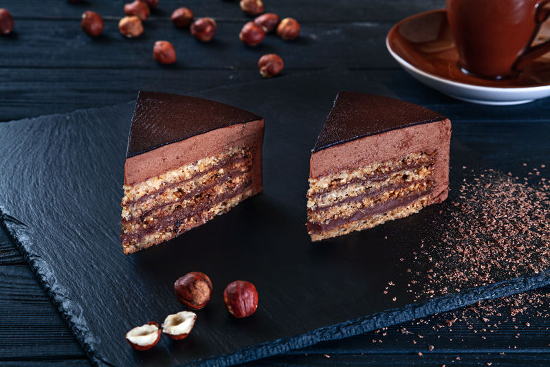 特写镜头在切片榛子蛋糕与可可在黑色背景和一个盘子-平铺糖果-图片-用于菜单、背景或带有复印空间的设计-甜点-巧克力蛋糕
