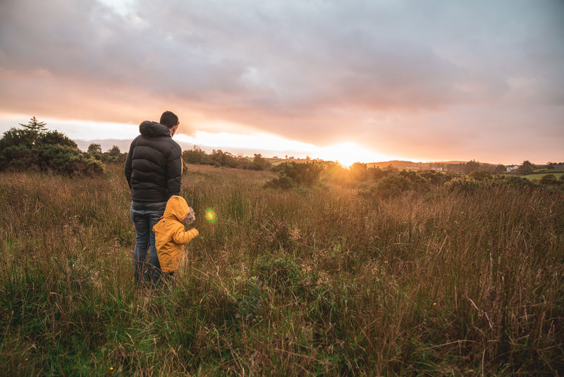 日落时分在草地上抱着孩子的男子穿着黄色连帽衫