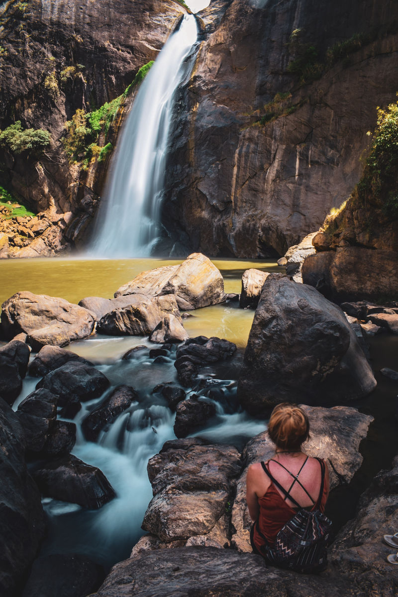 坐在棕色岩石上看瀑布的女人
