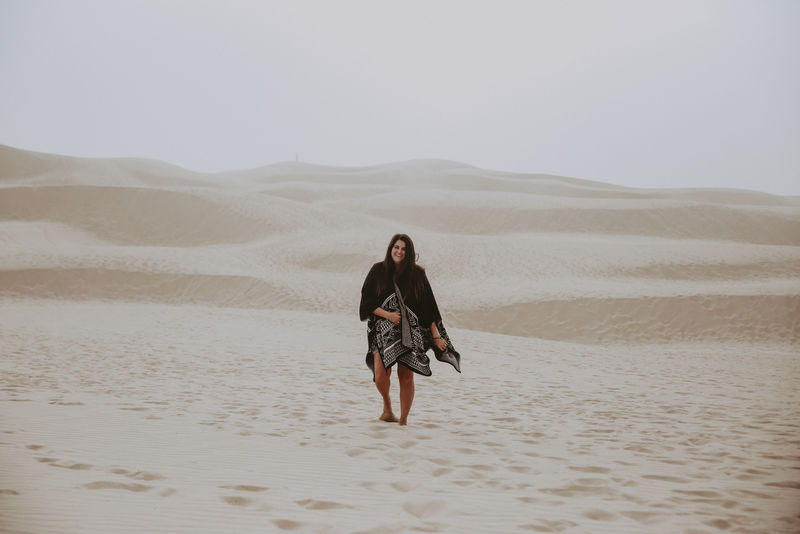 穿黑灰色斗篷在沙漠中行走的女人