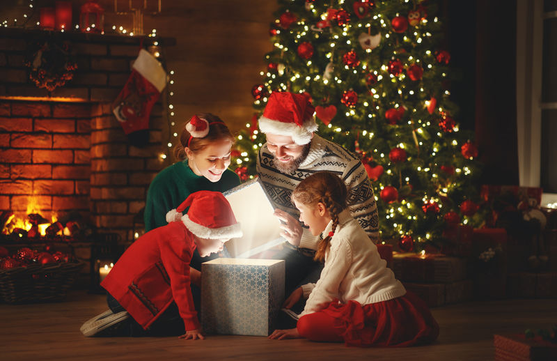 圣诞快乐！快乐的家庭母亲父亲和孩子晚上在家里的树附近带着魔法礼物