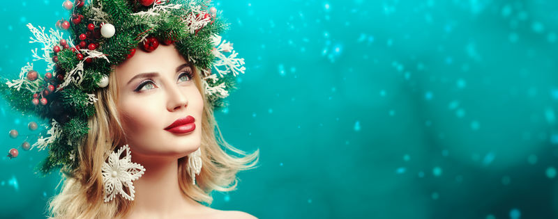 圣诞冬日美女-美丽快乐的年轻女子头上戴着圣诞松树花圈-装饰着圣诞球、浆果和雪花-圣诞绿背景上的画室肖像