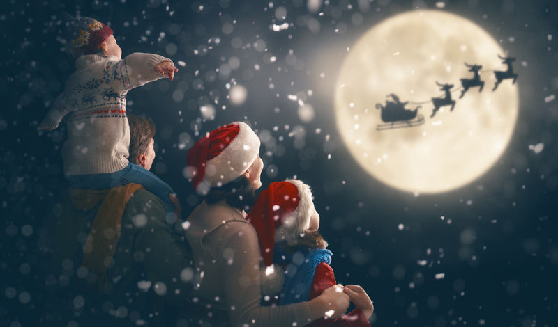 圣诞快乐-节日快乐！可爱的孩子和爸爸妈妈-圣诞老人驾着雪橇飞向月亮的天空-一家人在黑暗的背景下享受假期