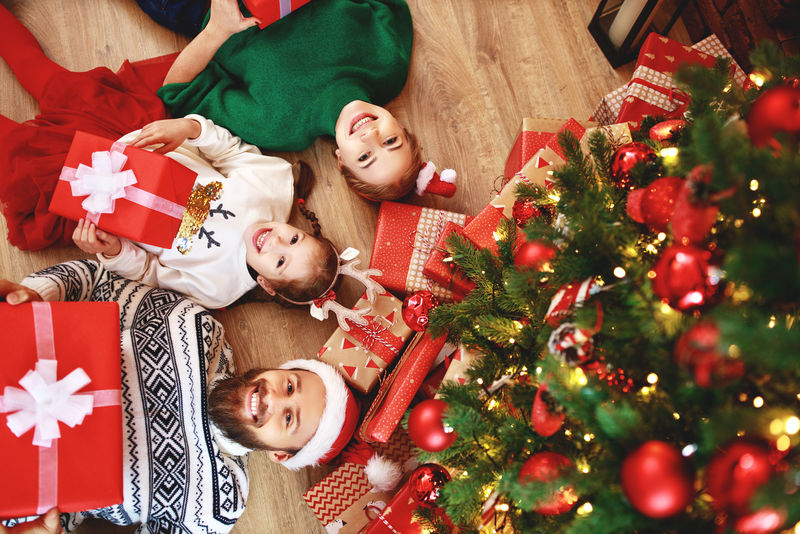 家里圣诞树旁带着礼物的幸福家庭父母和孩子