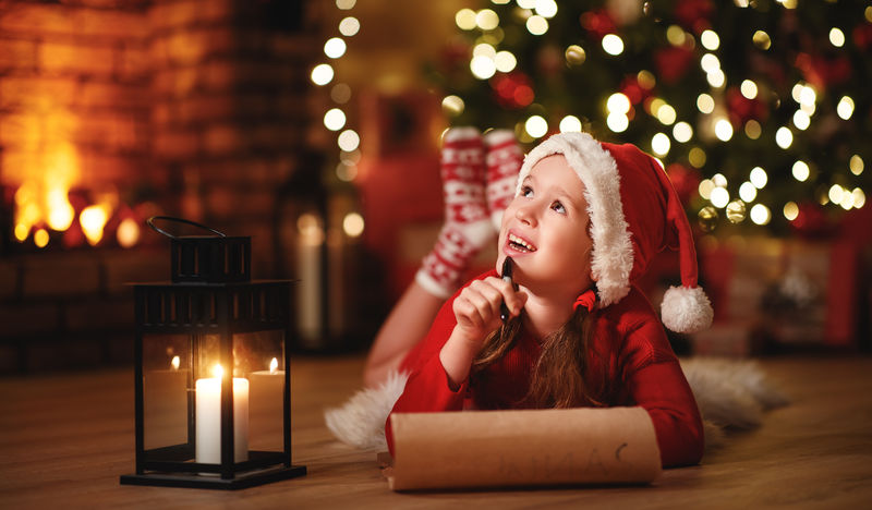 快乐的小女孩在圣诞树旁写信给圣诞老人家