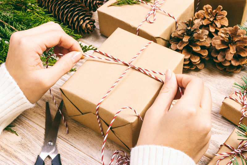 女人包装圣诞礼物，女孩准备圣诞礼物与杉树和松果。木制背景手工制作的圣诞礼物。俯视图，复制空间。柔和的
