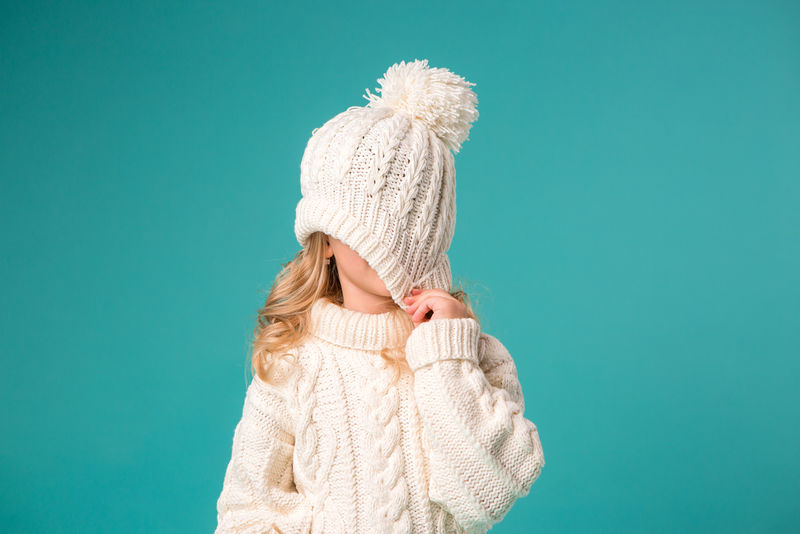 金发小女孩在白色冬季针织帽和蓝色背景隔离毛衣-空间文字-孩子们在冬天和雪中快乐-冬装