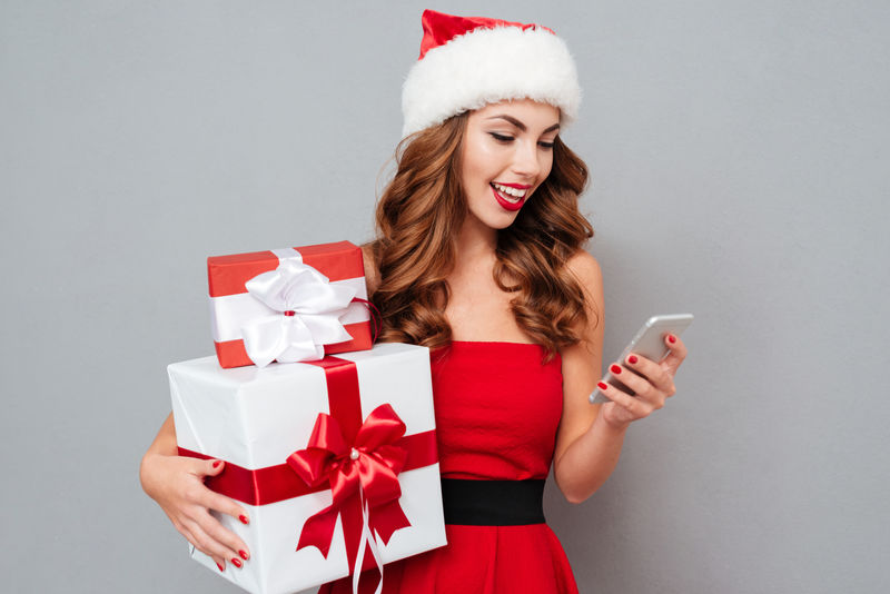 微笑的女孩拿着圣诞礼物看手机