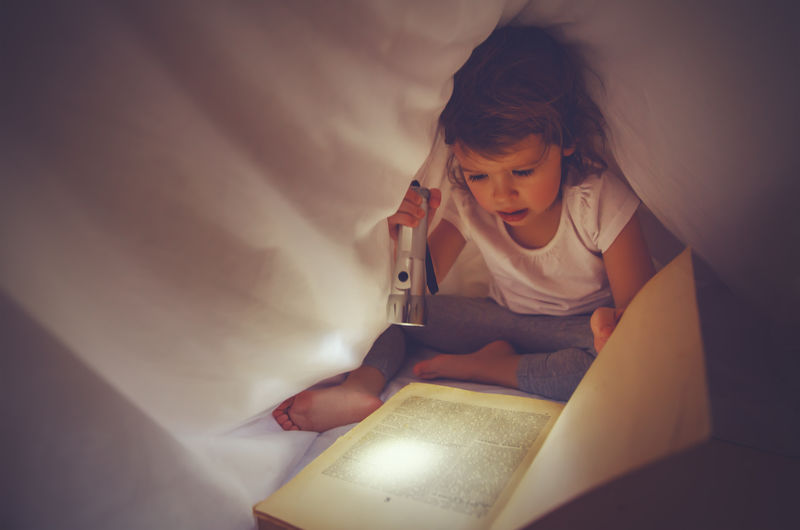 女孩在黑暗中看书，在床上用光遮盖