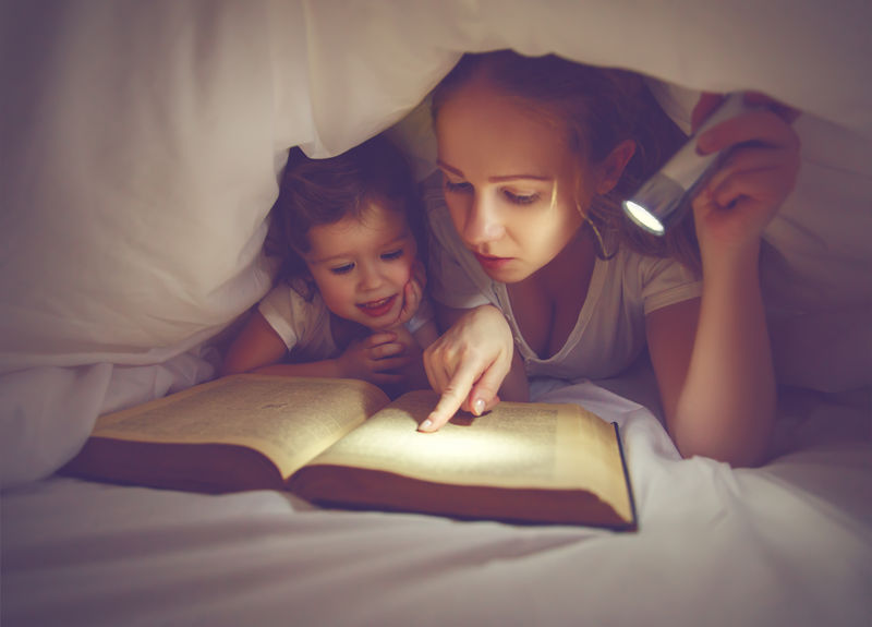 家庭阅读就寝时间。带闪光灯的妈妈和孩子读书