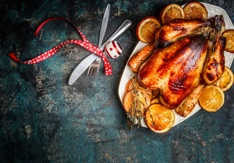 烤火鸡或鸡肉，盘中有橘子片，在黑暗中用叉子、刀子和节日装饰物供应圣诞晚餐。