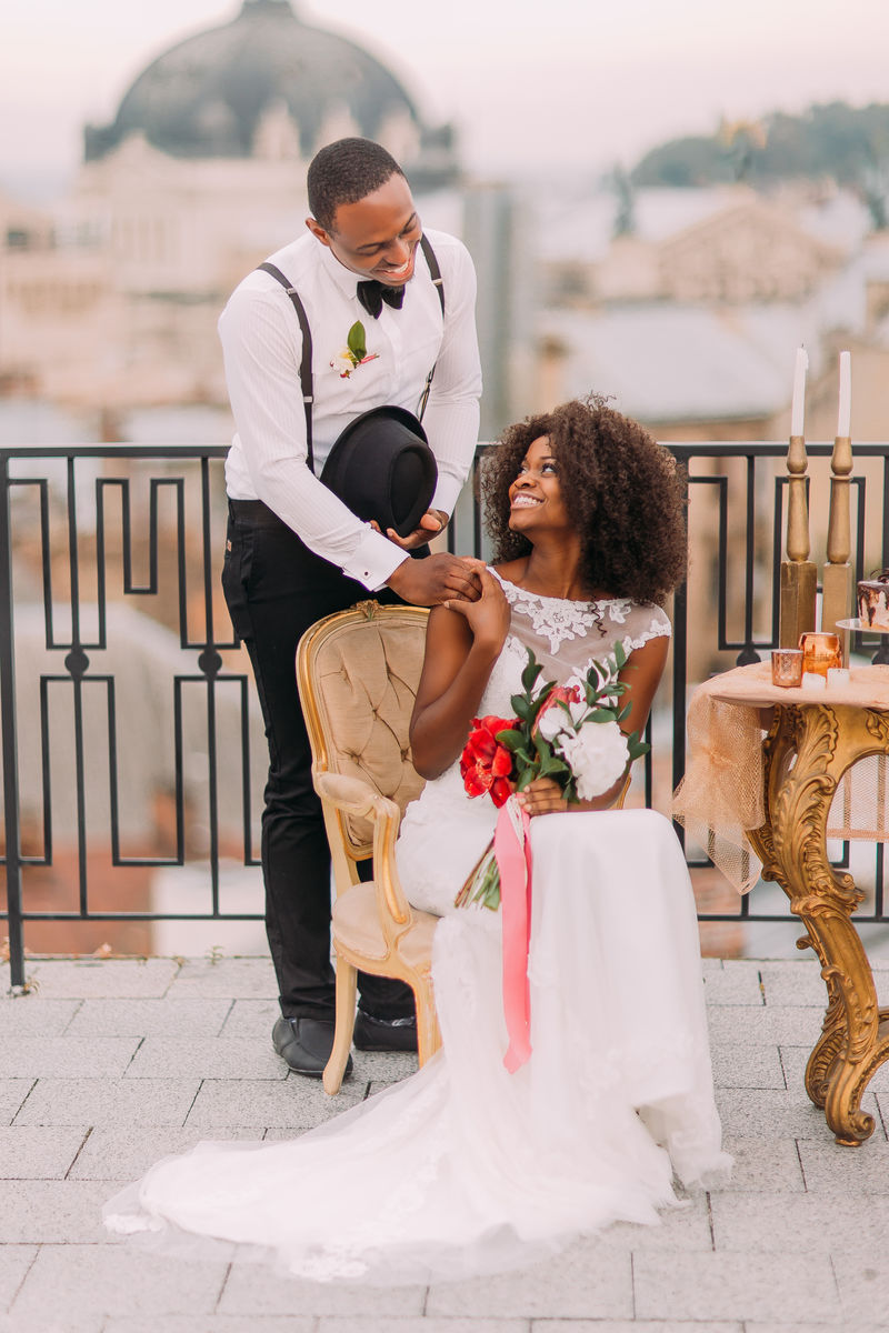 快乐的黑人新娘和新郎微笑着，手牵着手在露台上。结婚日